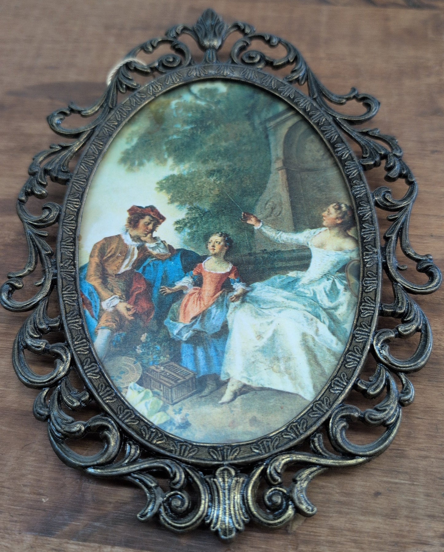 Rococo-style pastoral scene print in an ornate metal frame.