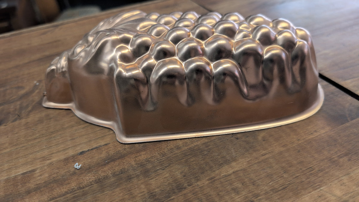 A vintage copper mold shaped like a cluster of grapes.